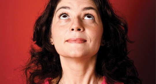 Imagem da neurocientista Suzana Herculano-Houzel equilibrando um pequeno cérebro de plástico em sua cabeça