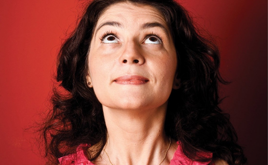 Imagem da neurocientista Suzana Herculano-Houzel equilibrando um pequeno cérebro de plástico em sua cabeça