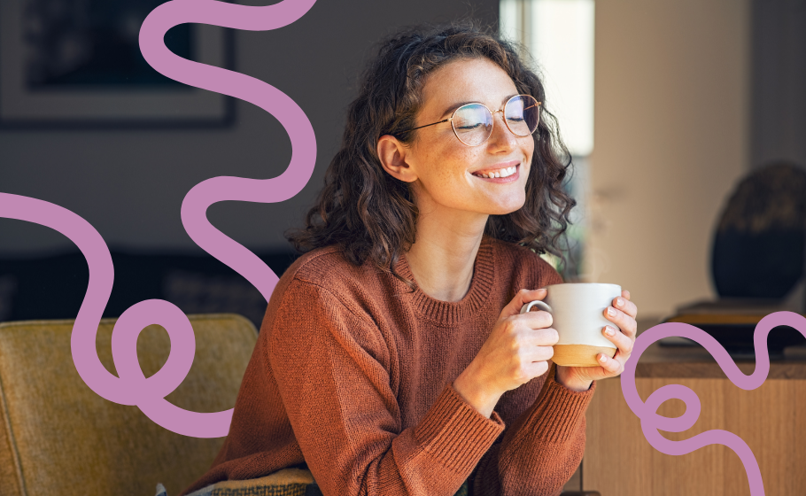 Arte mostra mulher jovem de cabelos soltos e cacheados, óculos de grau, vestindo um blusão de lã coral, com os olhos fechados e expressão relaxada diante de uma xícara de café