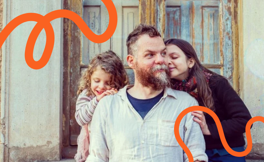 Arte mostra Marcos Piangers, um homem branco e com barba, ao lado das duas filhas, duas crianãs bancas abraçadas ao pai