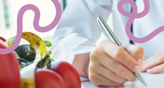 Imagem mostra mãos de médica de jaleco branco com uma caneta para prescrição, ao lado de tomates e alimentos