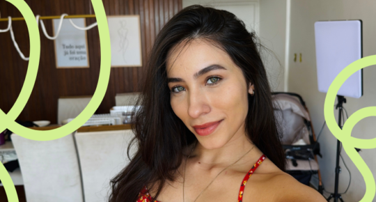 Foto no formato selfie de Isadora, mulher branca, com cabelos pretos e olhos claros. Ao fundo, o que parece ser um consultório médico.